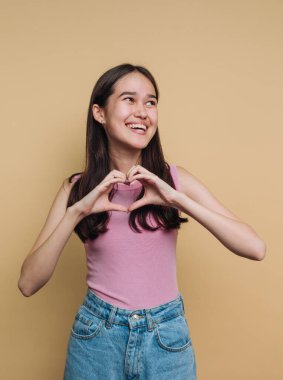 Gülümseyen kadın, bej arka planda elleri olan kalp şekli yapıyor..