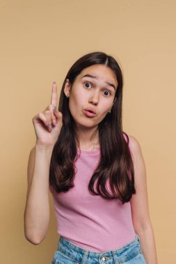 Pembe bluzlu genç bir kadın parmak kaldırarak şaşırmış bir ifade takınıyor..