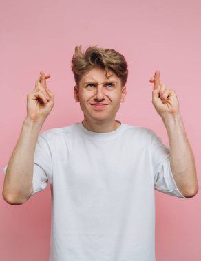 Beyaz gömlekli adam pembe arka planda parmaklarını çapraz yapıyor.