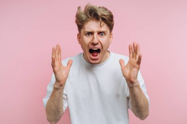 Pembe arka planda beyaz tişört giyen öfkeli bir genç adam..