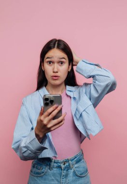 Pembe arka planda telefonuna şaşırmış genç bir kadın..