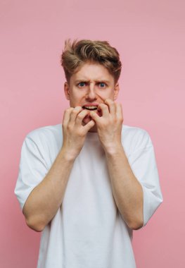 Pembe arka planda tırnak yiyen endişeli yüzlü genç adam..