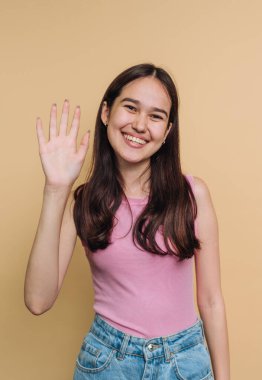 Gülümseyen genç bir kadın bej bir arka plana el sallıyor..