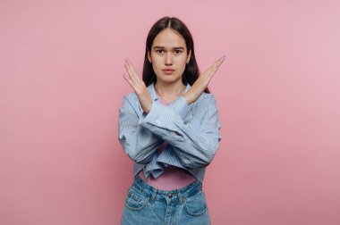 Genç bir kadın pembe arka planda kollarıyla X hareketi yapıyor..