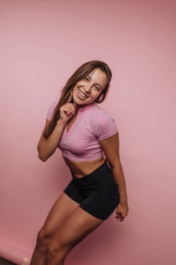 Pembe arka planda poz veren atletik giysili gülümseyen kadın.