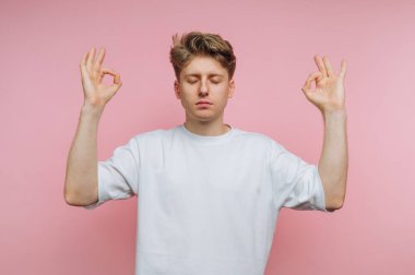 Genç adam pembe arka planda kapalı gözlerle meditasyon yapıyor.