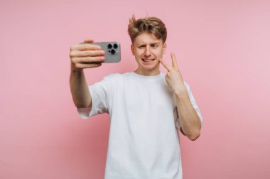 Genç bir adam pembe bir arka planda akıllı telefonuyla selfie çekiyor..