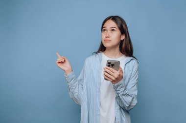 Elinde akıllı telefon tutan genç bir kadın, yukarı bakıyor, mavi arka plan..