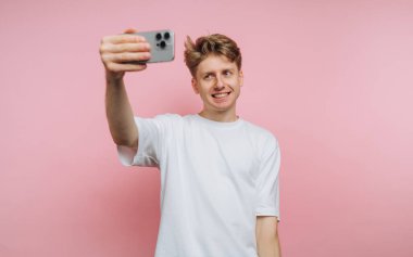 Pembe arka planda selfie çeken genç bir adam..