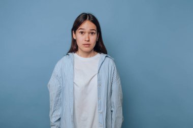 Mavi arka plana karşı tarafsız bir ifadeyle genç bir kadın..