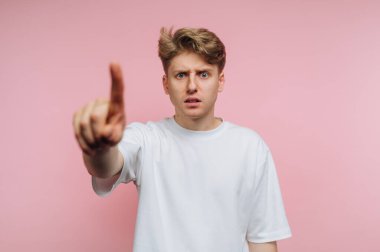 Beyaz tişörtlü genç bir adam şaşırmış bir ifadeyle işaret ediyor..