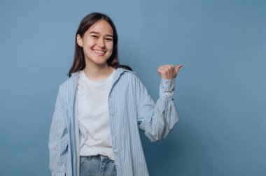 Genç bir kadın gülümsüyor ve mavi bir arka plana doğru işaret ediyor..