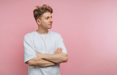 Pembe arka planda duran beyaz tişörtlü genç adam..