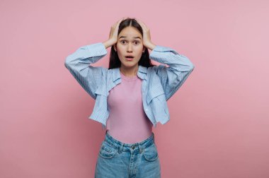 Pembe arka planda elleri başının üstünde şaşırmış genç bir kadın..