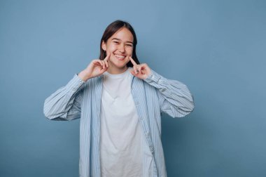 Gülümseyen genç bir kadın mavi arka planda yanaklarını gösteriyor..