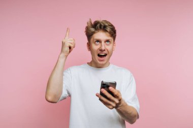 Akıllı bir telefon tutan heyecanlı genç adam, yukarıya bakıyor..