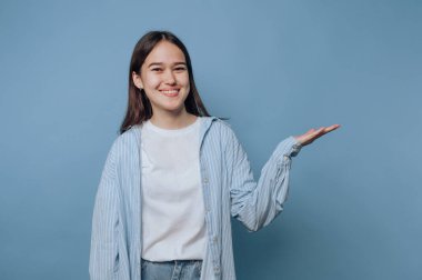 Gülümseyen genç bir kadın mavi arka planda el kol hareketi yapıyor..