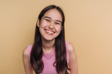 Bej arka planda pembe bluzlu, gülümseyen genç bir kadın..