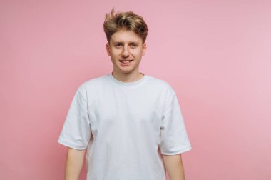 Beyaz tişörtlü genç adam pembe arka plana gülümsüyor..