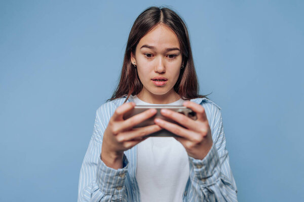 Young woman looking surprised at smartphone against blue background.
