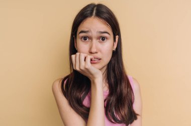 Genç bir kadın arka planda duruyor, tırnağını yiyerek kaygı gösteriyor. İleriye bakarken ifadesi belirsizliği ve düşünmeyi yansıtıyor..