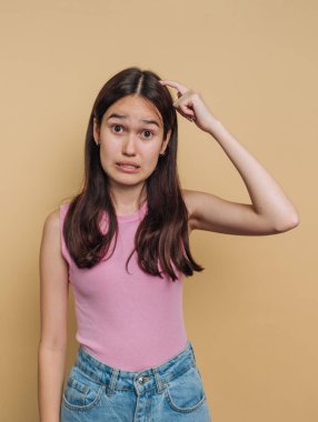 Genç bir kız sade bir arka planın önünde duruyor, şaşkın bir bakış ve kafasında bir el ile kafa karışıklığını ifade ediyor. Pembe bluz ve kot pantolon giyiyor, belli ki emin değil..