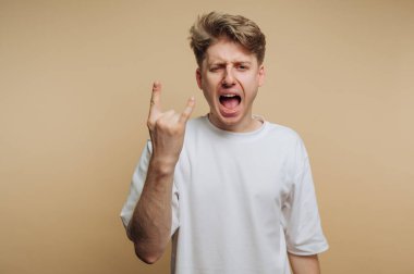 Genç bir adam coşkuyla bağırırken, bir stüdyo ortamında şen şakrak ve enerjik bir tavır sergilerken, sert bir el hareketi yapar..