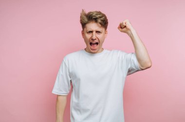 Genç bir adam yumruğunu kaldırıp sevinçle bağırarak heyecan gösteriyor. Canlı pembe bir arka plana karşı duruyor, saf bir coşku anı yakalıyor..