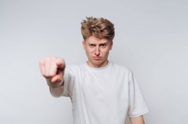 Genç bir adam düz bir arkaplan önünde duruyor, açıkça hayal kırıklığına uğramış bir şekilde doğrudan kameraya doğru sert bir ifadeyle bakıyor, mesajını ilgi çekici bir şekilde vurguluyor..