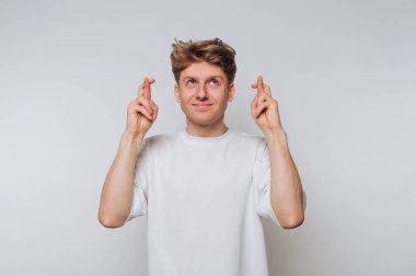 Genç bir adam arka planda duruyor, neşeli bir jest yapmak için parmaklarını çapraz yapıyor. Yüzünde neşe dolu bir gülümseme var, iyimserliği ve iyimserliği gösteriyor..