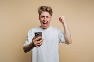Genç bir adam, zaferle yükselen akıllı telefonuna bakarken heyecanını ve neşesini ifade ediyor. Tepkisi yeni bir başarı ya da başarı olduğunu gösteriyor..