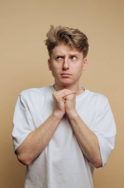 Genç bir adam elleri sımsıkı bağlı, endişeli bir ifade sergiliyor. Saçı dağınık ve beyaz gömleği sıcak, tarafsız arka plana karşıydı. Endişesini vurguladı..