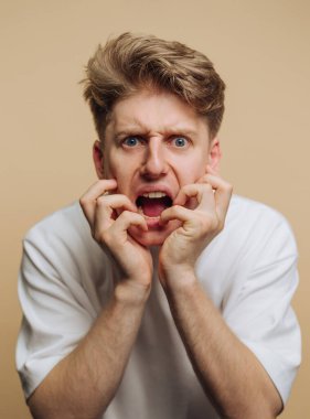 Genç bir birey iki eliyle yüzünü tutarak güçlü duygular ifade eder. Tarafsız arkaplan, tasvir edilen duyguyu arttırır. Yükselen bir dramın görüntüsü..