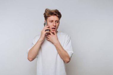 Bir an gafil avlanan beyaz tişörtlü genç bir adam kulağına bir akıllı telefon dayadı. Düz bir zemine karşı dururken endişe belirtileri gösteriyordu..