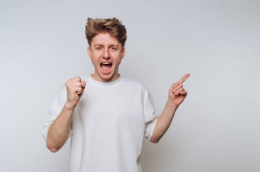 Sarı saçlı genç bir adam sevinç ve heyecan ifade eder. Yumruğunu kaldırır ve gün boyunca kapalı bir ortamda gülümseyerek işaret eder..