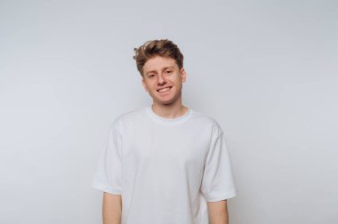 Genç bir adam basit bir beyaz zemine karşı duruyor, içten bir gülümsemeyle. Günlük kıyafetleri ve arkadaş canlısı ifadesi davetkar bir atmosfer yaratıyor. Kişisel markalaşma için mükemmel..