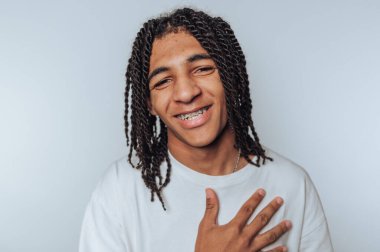 Rasta ve diş telleriyle gülümseyen genç adam, beyaz bir gömlek giyiyor..