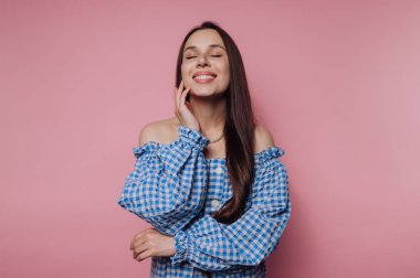 Mavi elbiseli gülümseyen kadın pembe arka planda omuzları kapalı..