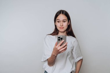 Beyaz gömlekli genç bir kadın arka planda akıllı telefon kullanıyor..