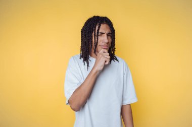 Saçları örgülü, sarı arka planı düşünen genç bir adam..