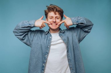 Kot gömlekli genç adam gülümsüyor ve gülüşünü gösteriyor..