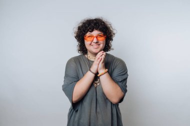 Kıvırcık saçlı, turuncu güneş gözlüklü ve gri gömlekli biri.