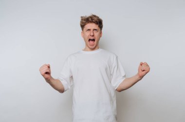 Beyaz tişörtlü genç bir adam. Yumruklarını sıkarak heyecanını ifade ediyor..