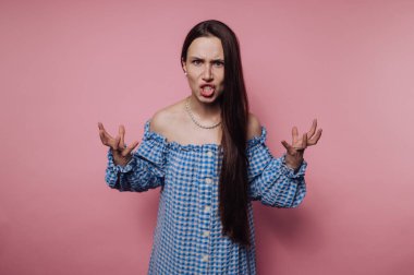 Mavi elbiseli kadın pembe arka plana karşı öfkesini dile getiriyor..