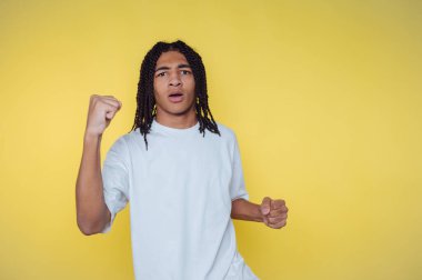 Sarı arka planda beyaz gömlekli örgülü genç bir adam..