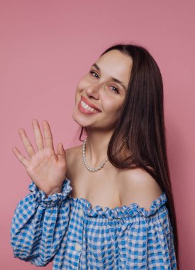 Gülümseyen kadın pembe bir arka plana el sallıyor.