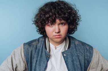 Kıvırcık saçlı, mavi arka planda kot ceket giyen biri..