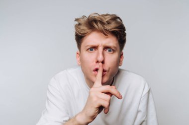 Parmakları dudaklarında, gri arka planda sessizlik sinyali veren bir adam..