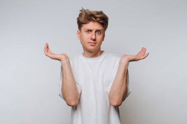 Beyaz tişörtlü, kafası karışmış genç bir adam omuz silkiyor..