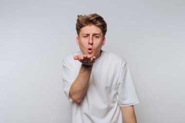 Beyaz tişörtlü genç adam gri bir arka plana öpücük yolluyor..